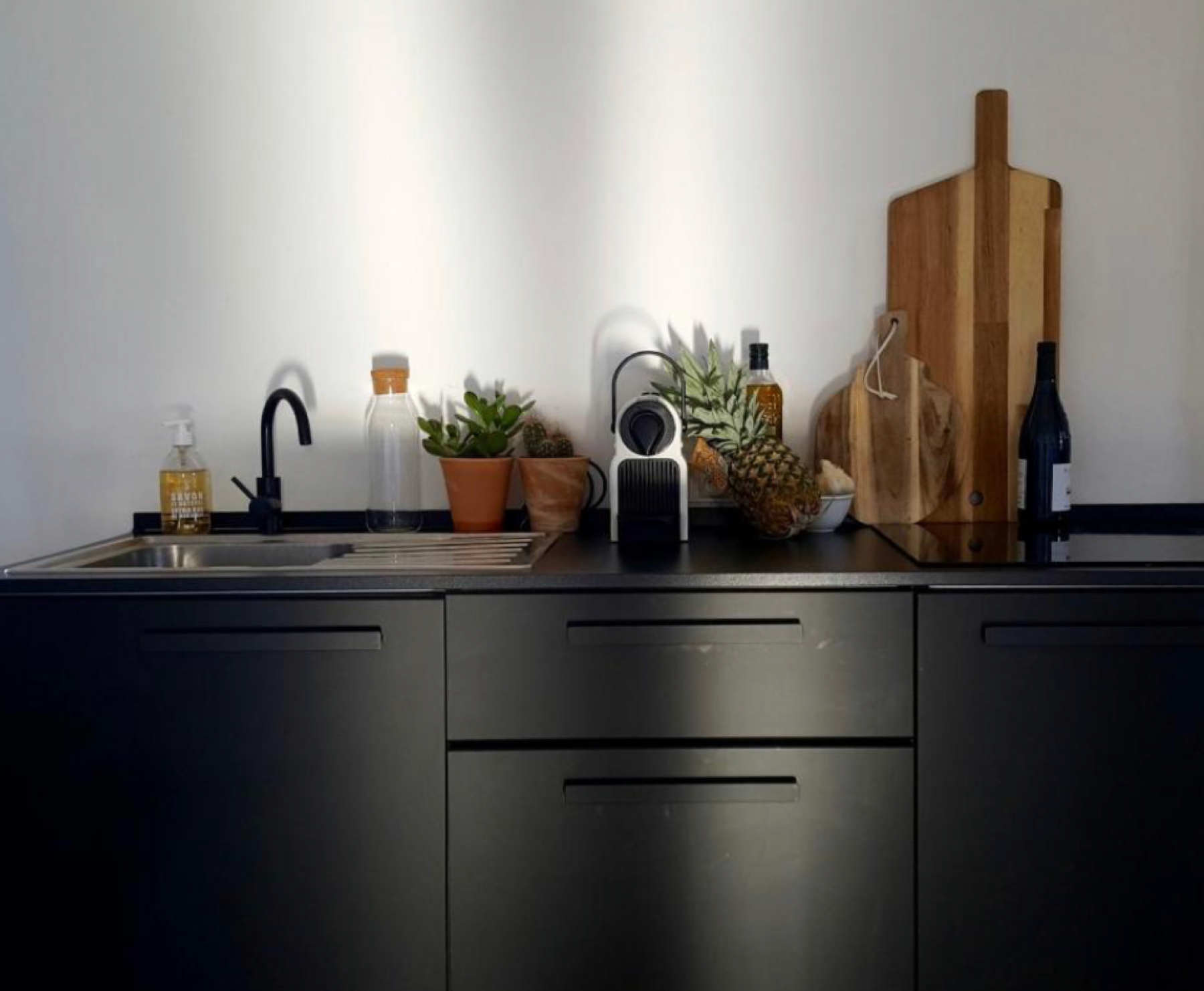 Kitchenette noire avec évier, machine à café, planches à découper et plantes, Appartement 4