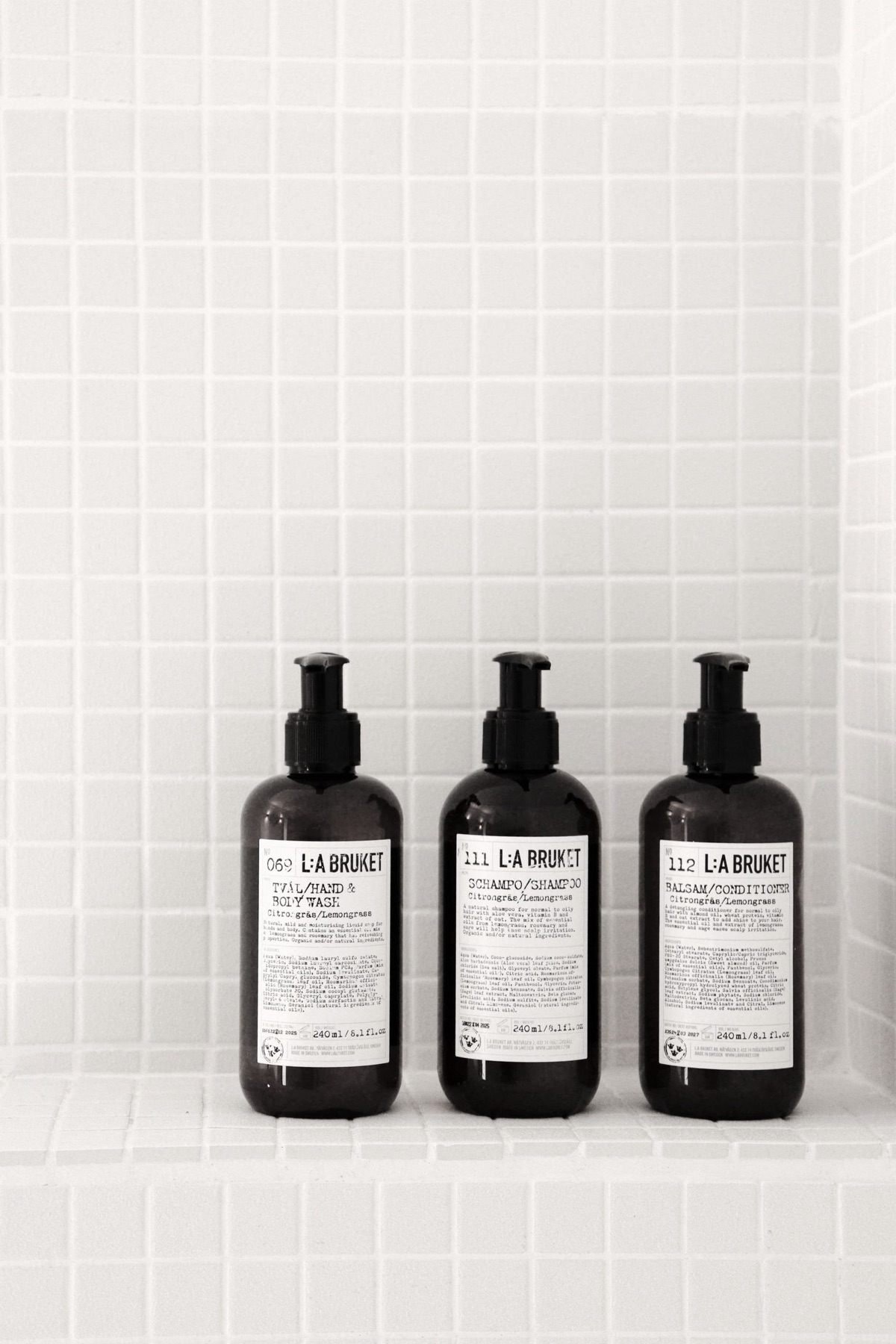 Trois flacons de produits de toilette sur la tablette d'une douche carrelée de blanc, Appartement 4