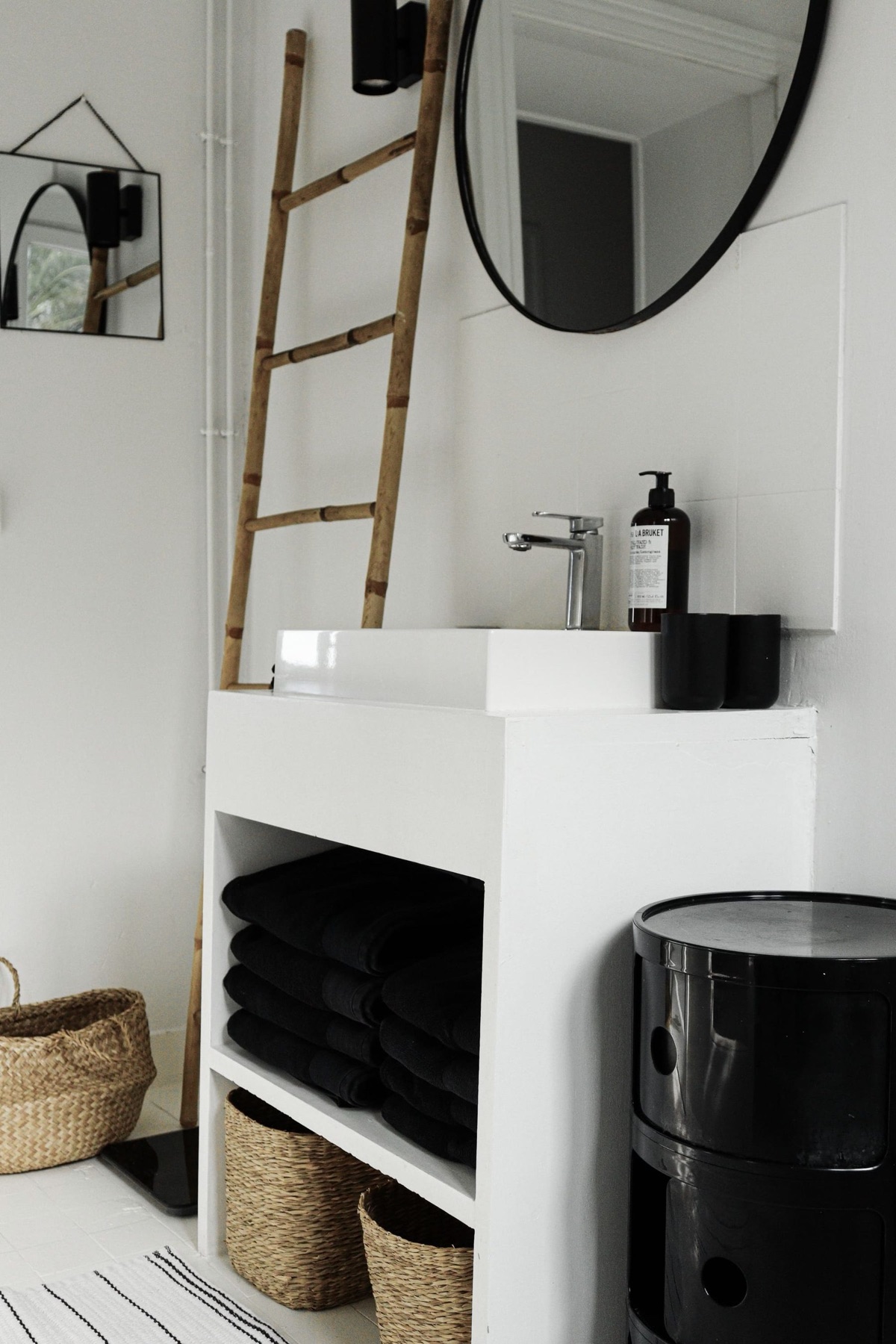 Vasque blanche, échelle en bambou, paniers et serviettes noires dans la salle de bain de l'Appartement 4